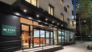 A modern hotel exterior with large glass windows, a visible seating area inside, and a sign indicating the hotel name. - EVEN Hotel Long Island City - New York by IHG (Long Island City)