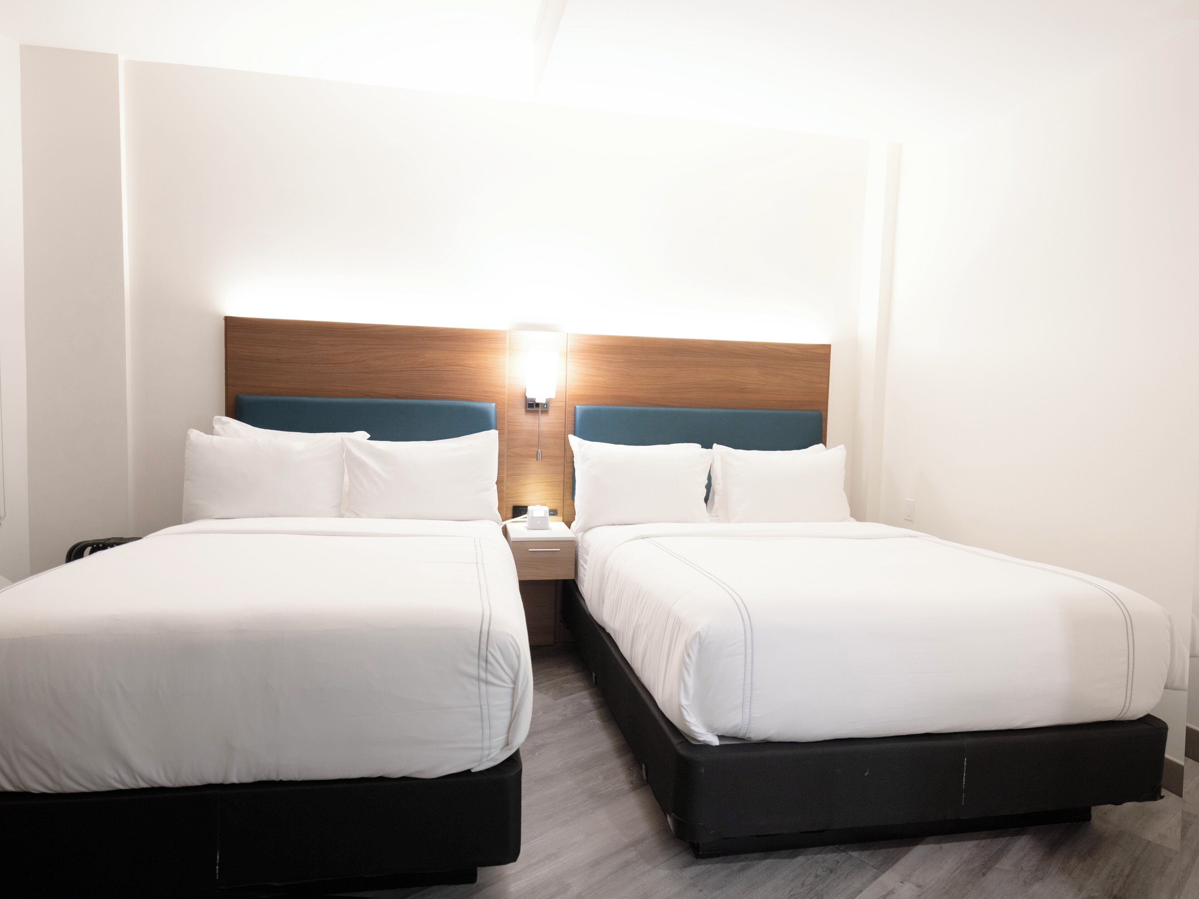 Habitación de hotel con dos camas, cada una con ropa blanca y cabeceros de madera.
