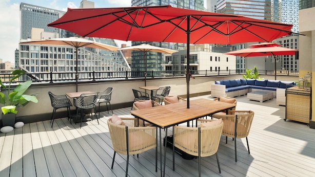 A rooftop terrace with outdoor seating, including tables and chairs, and red umbrellas. - EVEN Hotel Long Island City - New York by IHG (Long Island City)