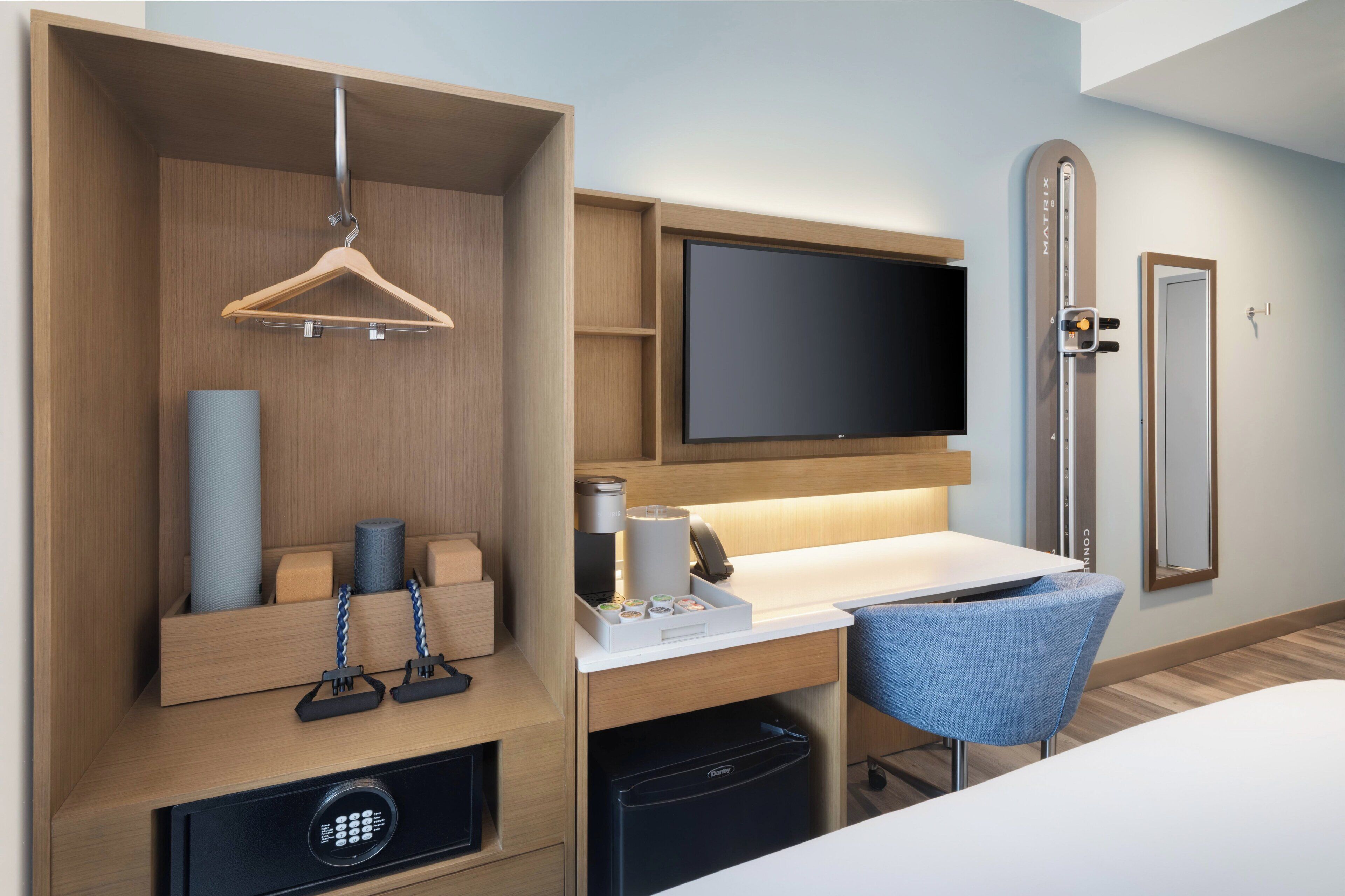 Una habitación de hotel con un armario de madera, un escritorio con silla, un televisor de pantalla plana y un minibar.