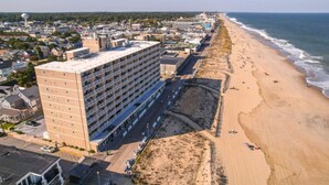 A high-rise hotel with multiple floors and balconies, adjacent to a sandy beach with a few people and a clear view of the ocean. - Ocean View Escape Studio Condo (Rehoboth Beach)