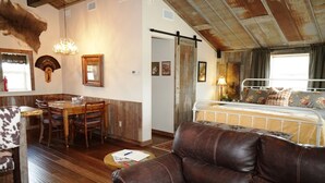 Un interno rustico con zona pranzo, divano in pelle e un letto con lenzuola a motivi floreali.