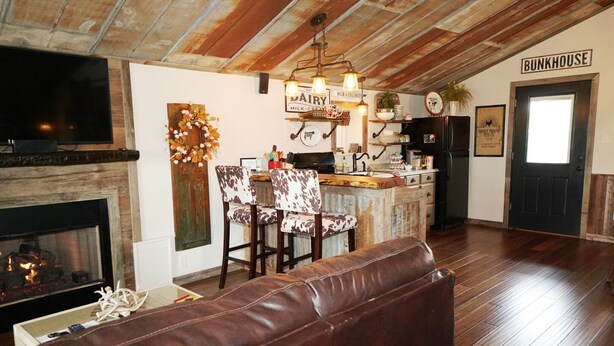 Un accogliente soggiorno con camino, soffitto in legno, angolo bar e un cartello con su scritto "BUNKHOUSE".