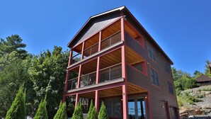 A multi-story building with a wooden facade and red accents, featuring balconies and large windows. - La Bella Vita in Bolton Landing (Bolton Landing)