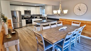 A modern kitchen with stainless steel appliances, a wooden dining table, and a clock on the wall. - La Bella Vita in Bolton Landing (Bolton Landing)