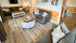 A spacious living room with a wooden floor, two grey sofas with patterned cushions, a white coffee table, and a television mounted on the wall. - La Bella Vita in Bolton Landing (Bolton Landing)