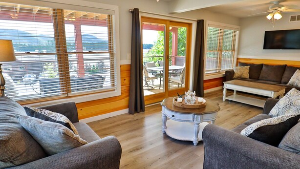 A spacious living room with a sofa, armchair, and coffee table. Large windows with blinds offer a view of the outdoors. - La Bella Vita in Bolton Landing (Bolton Landing)
