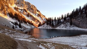 Eine natürliche Landschaft mit einem See, schneebedecktem Boden und einem felsigen Berg.