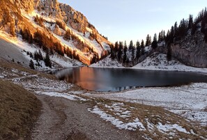 Eine natürliche Landschaft mit einem See, schneebedecktem Boden und einem felsigen Berg.