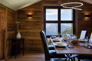 A dining area with a wooden interior, a large window with a mountain view, and a modern pendant light.