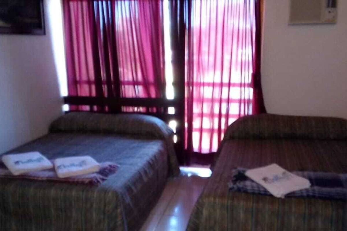 Une chambre avec deux lits, une petite table et une fenêtre avec des rideaux.
