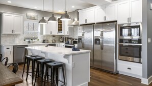 Una cocina moderna con armarios blancos, electrodomésticos de acero inoxidable y una isla central con taburetes de bar.