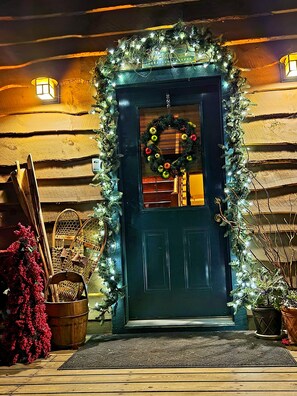 Une porte bleu foncé ornée d’une guirlande, entourée de guirlandes lumineuses et de décorations végétales.
