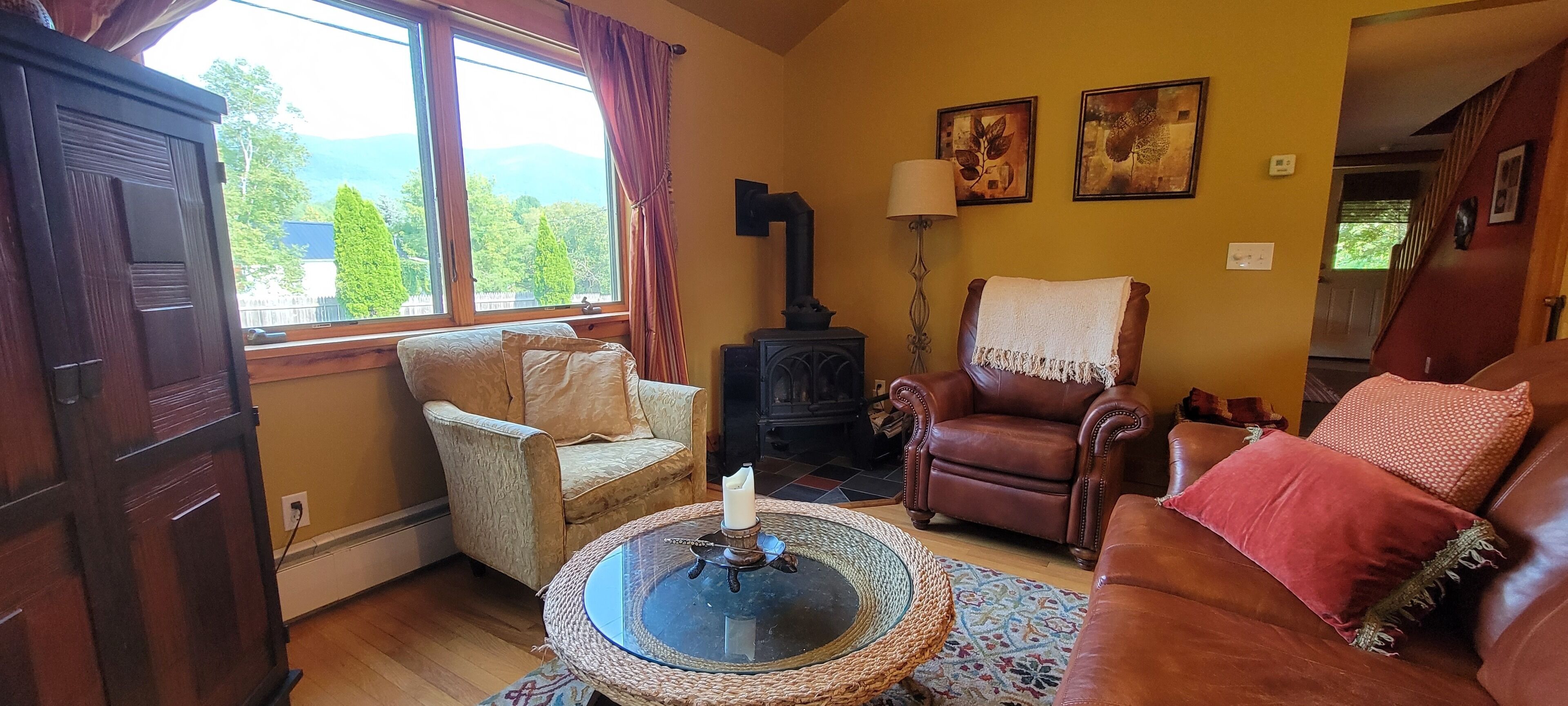 Un salon chaleureux avec une cheminée, des canapés en cuir, une table basse ronde et une vue sur la verdure à l’extérieur.