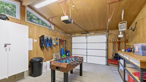 A room with a foosball table, a garage door, and various tools and equipment on shelves. - Scenic House Located At The Doorstep to West Glacier National Park Entrance
 (West Glacier)