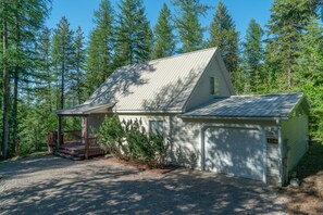 A single-story cabin with a covered porch, a garage, and a gravel driveway.