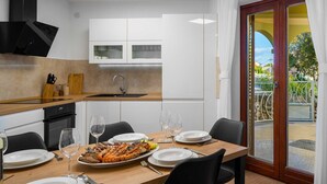 Una cocina moderna con comedor, que cuenta con una mesa grande dispuesta para dos personas, horno empotrado y vista al exterior por medio de un ventanal.