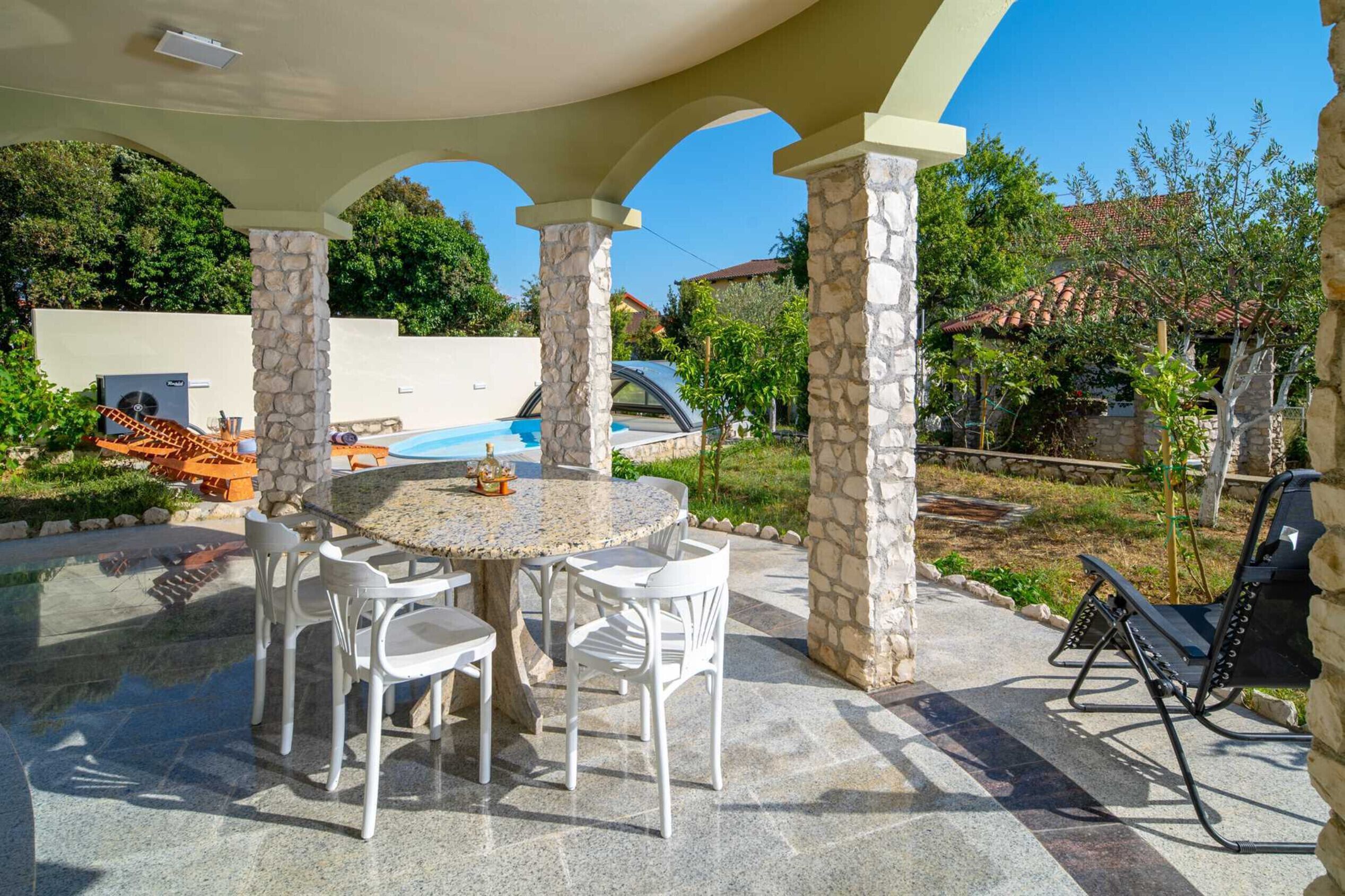 Un patio al aire libre con una mesa redonda y sillas, una piscina y un área de barbacoa.
