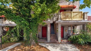 Un edificio de dos pisos con una puerta roja, un balcón de madera y una escalera que sube al segundo piso.