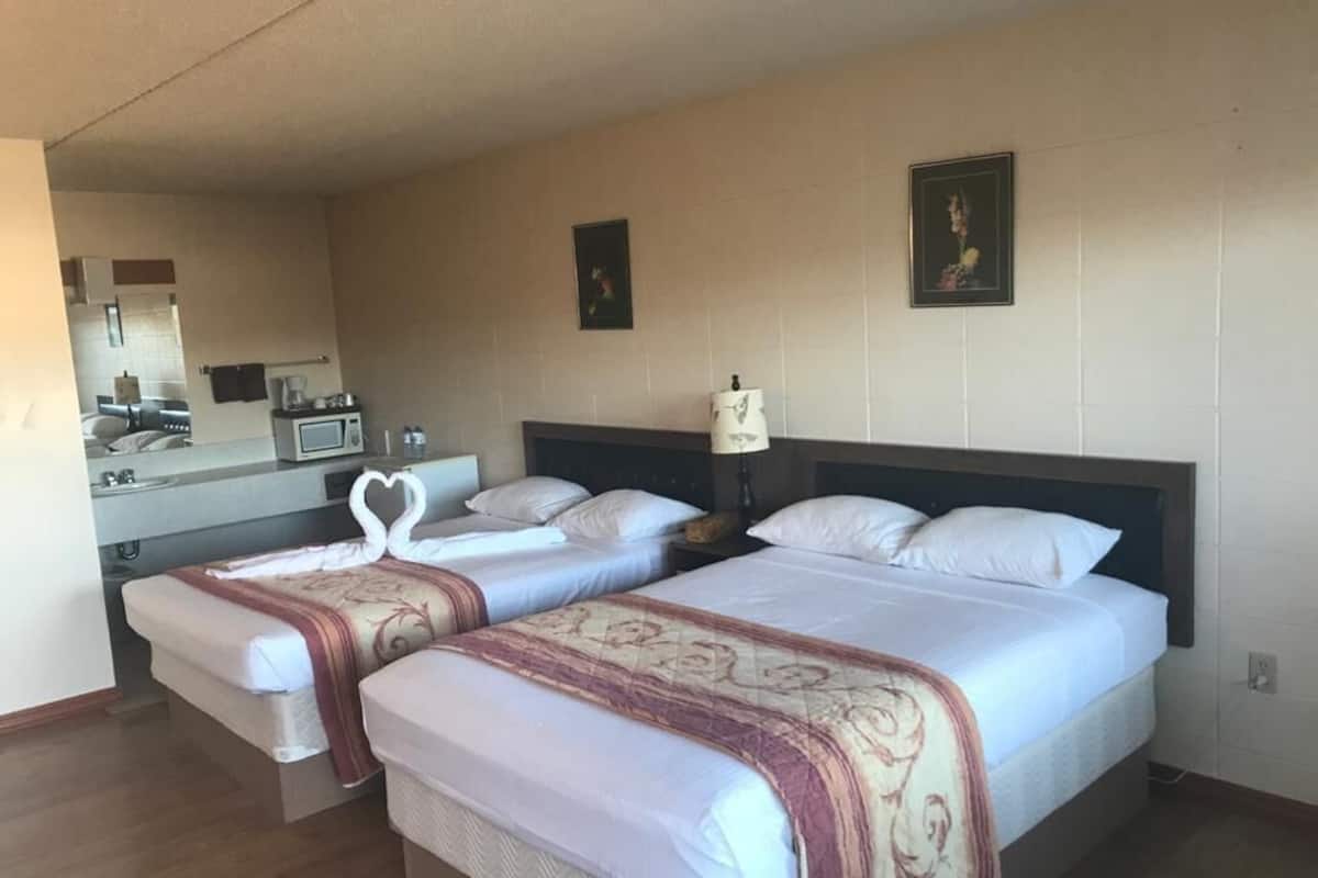 Habitación de hotel con dos camas, una kitchenette pequeña, un espejo y un cuadro en la pared.