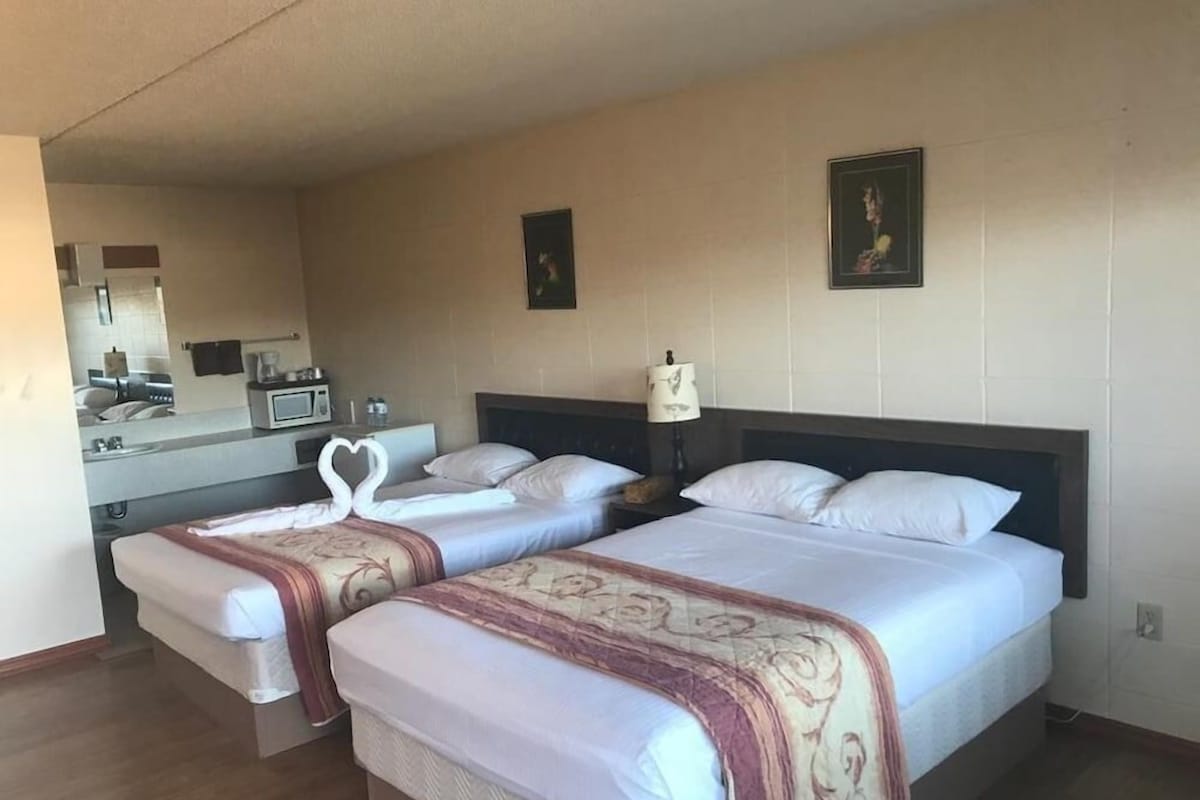 A hotel room with two beds, a small kitchenette, a mirror, and a framed picture on the wall.