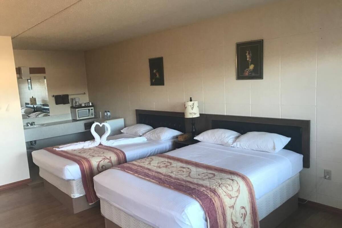 Habitación de hotel con dos camas, una kitchenette pequeña, un espejo y un cuadro en la pared.