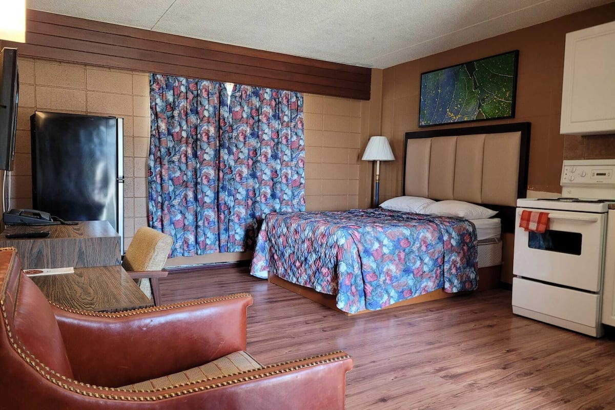 Habitación de hotel con cama, escritorio con televisor, silla, lámpara y estufa.