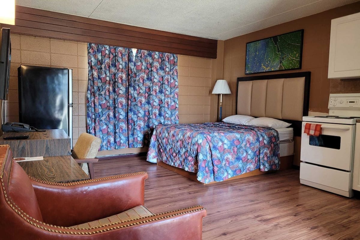 Habitación de hotel con cama, una silla, televisor, lámpara y horno.