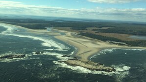 Ilmakuva rannikkoalueesta, jossa on hiekkarantoja, kallioita ja joki, joka virtaa maiseman halki.