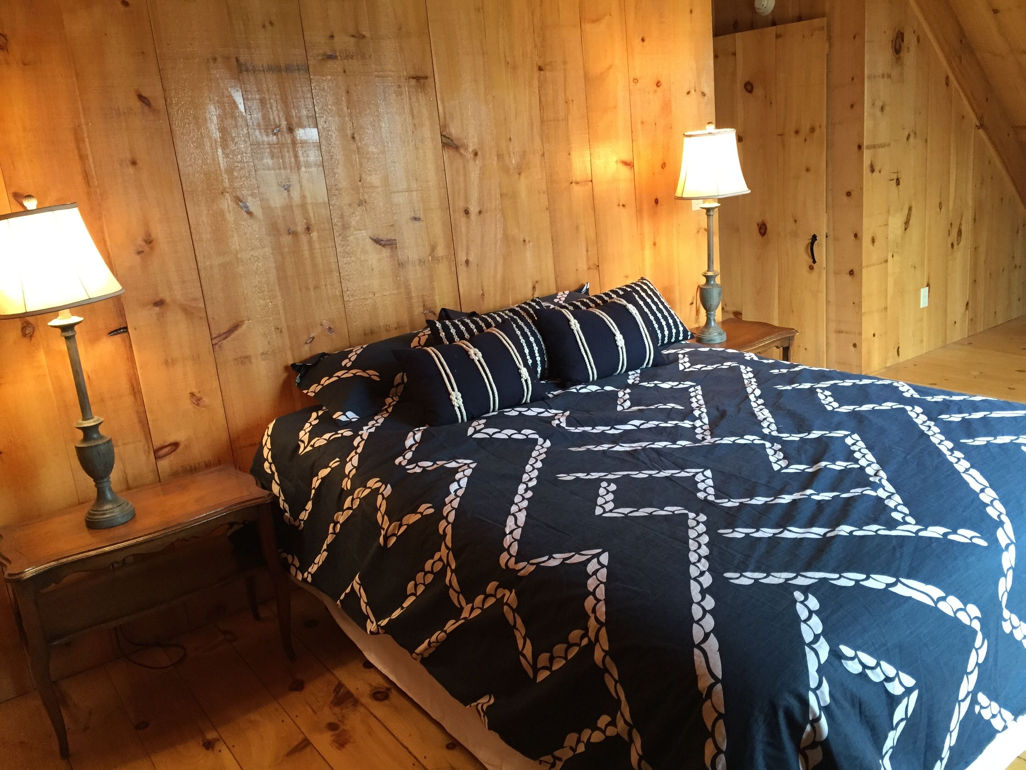 A wooden room with a bed, two nightstands, and two lamps.