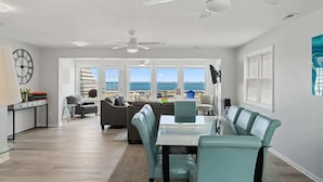 A spacious living area with a dining table, seating, and a view of the ocean. - Ocean Oasis by Carolina Getaway - Oceanfront Townhome w/ Private Heated Pool (Kure Beach)