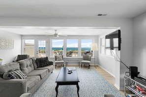A living room with a sofa, chairs, a coffee table, a TV, and a balcony with a view.