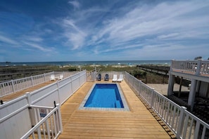 Um deck de madeira com piscina, guarda-corpos brancos e espreguiçadeiras.