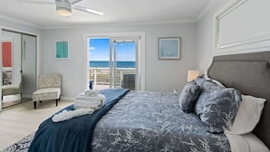 A bedroom with a bed, a ceiling fan, a chair, a window with a view, and a door. - Ocean Oasis by Carolina Getaway - Oceanfront Townhome w/ Private Heated Pool (Kure Beach)