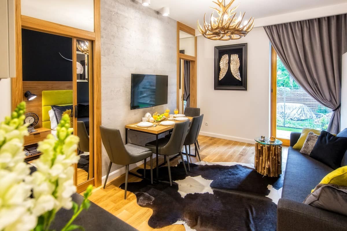 A modern living room with a dining area, a mounted TV, and a large window with curtains.