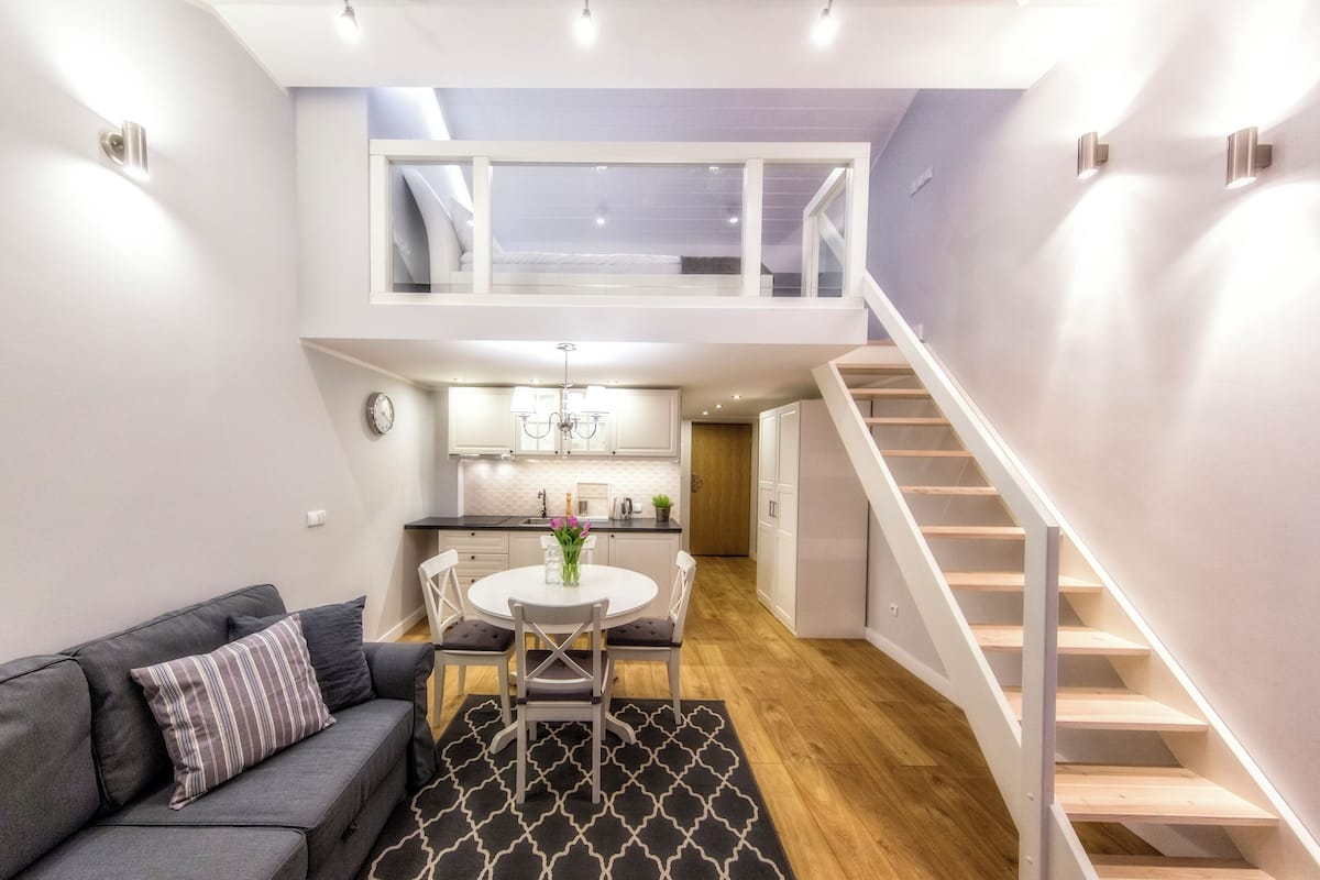 A modern apartment with a loft bedroom, a kitchen with white cabinets, and a staircase.