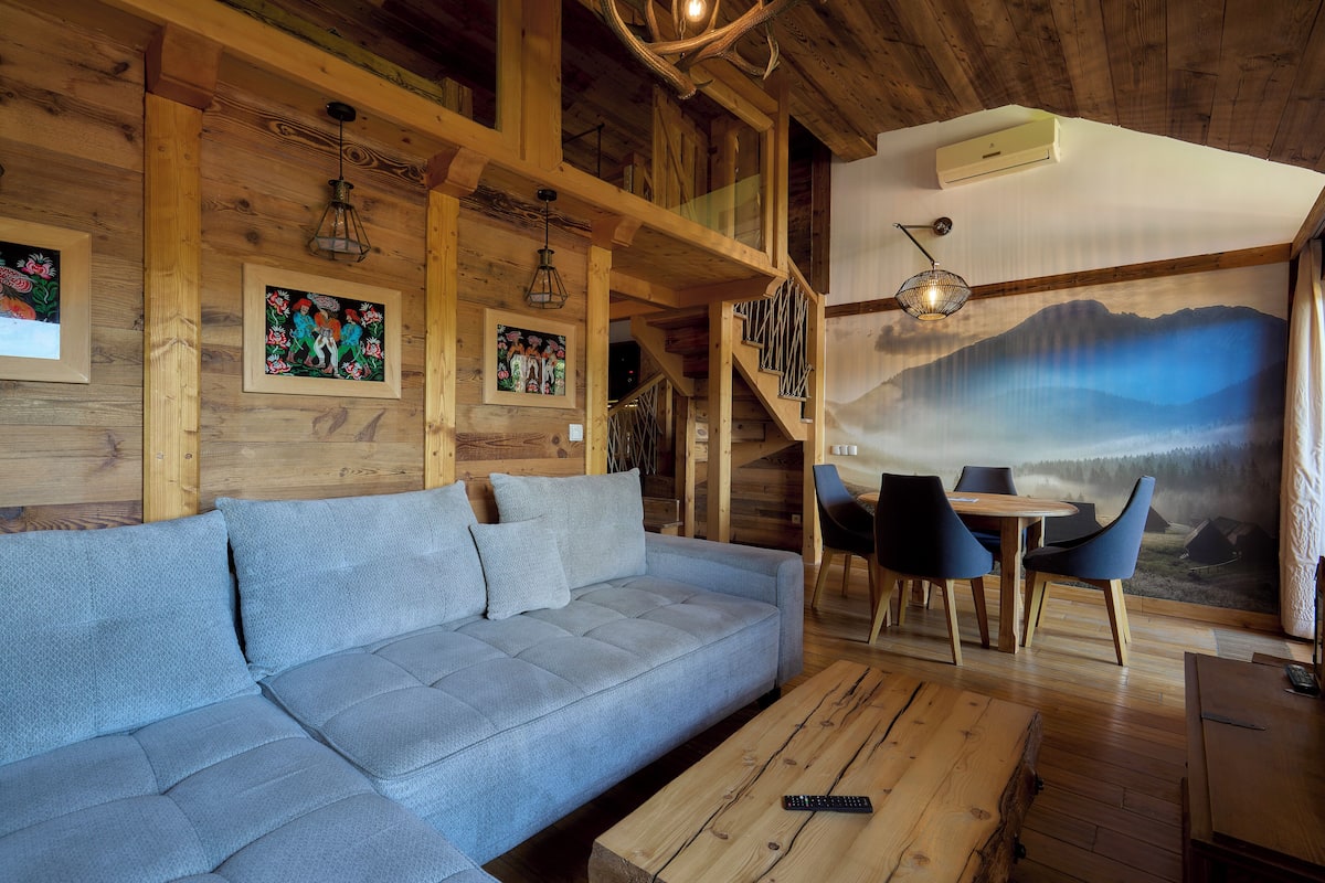 A wooden interior with a sofa, chairs, a table, and a staircase.