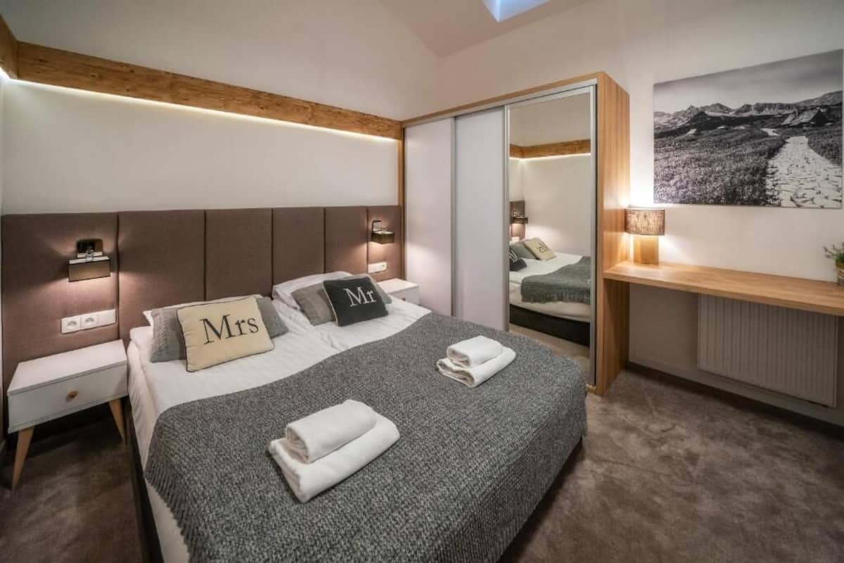 A modern bedroom with a large bed, bedside tables, a mirror, and a desk with a lamp.
