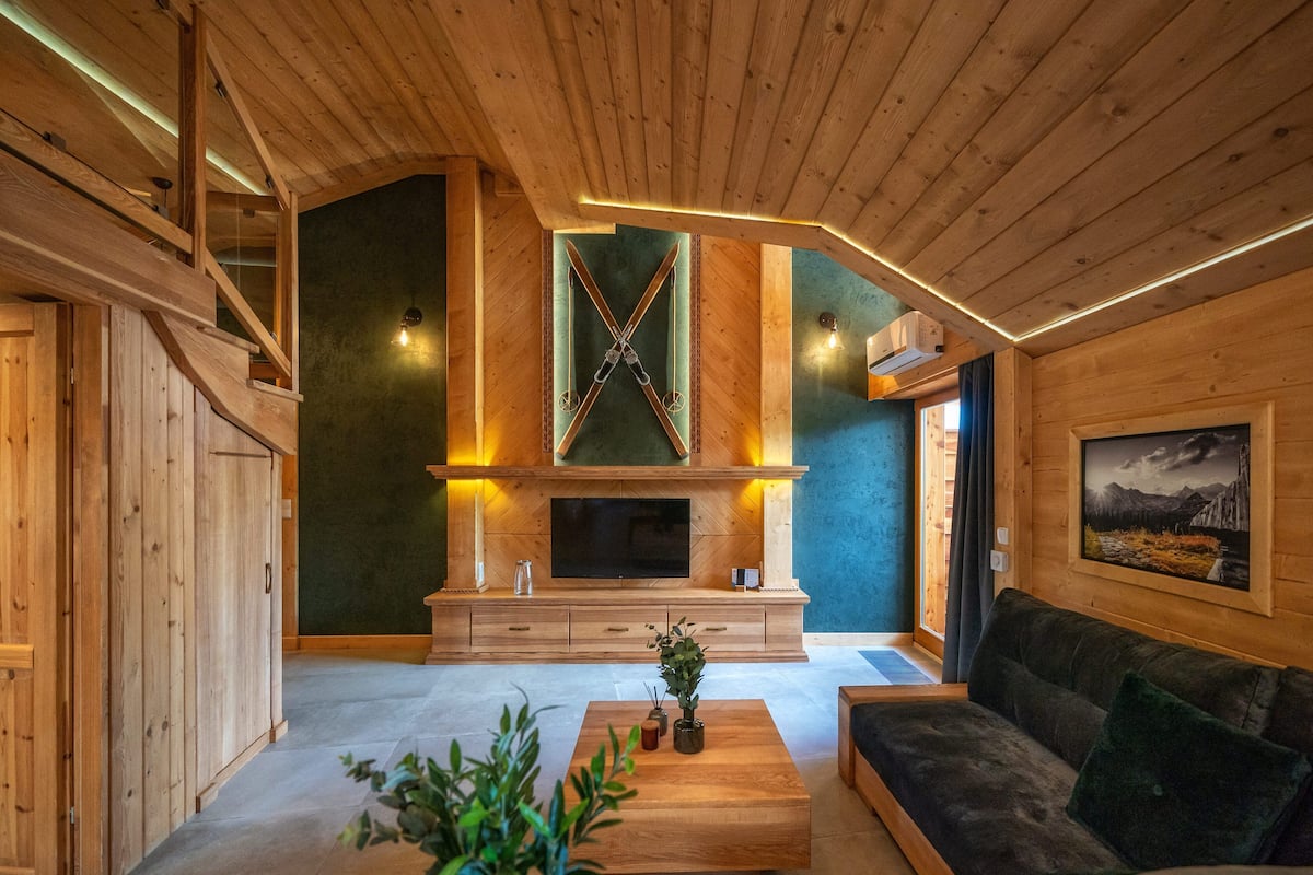 A modern living room with a wooden ceiling, a fireplace, a television, and a sofa.