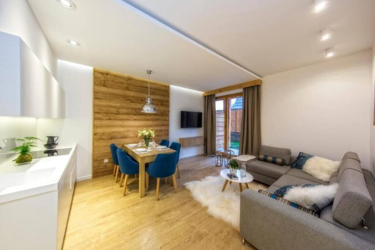 A modern living room with a grey sofa, a dining table with blue chairs, and a wooden accent wall.