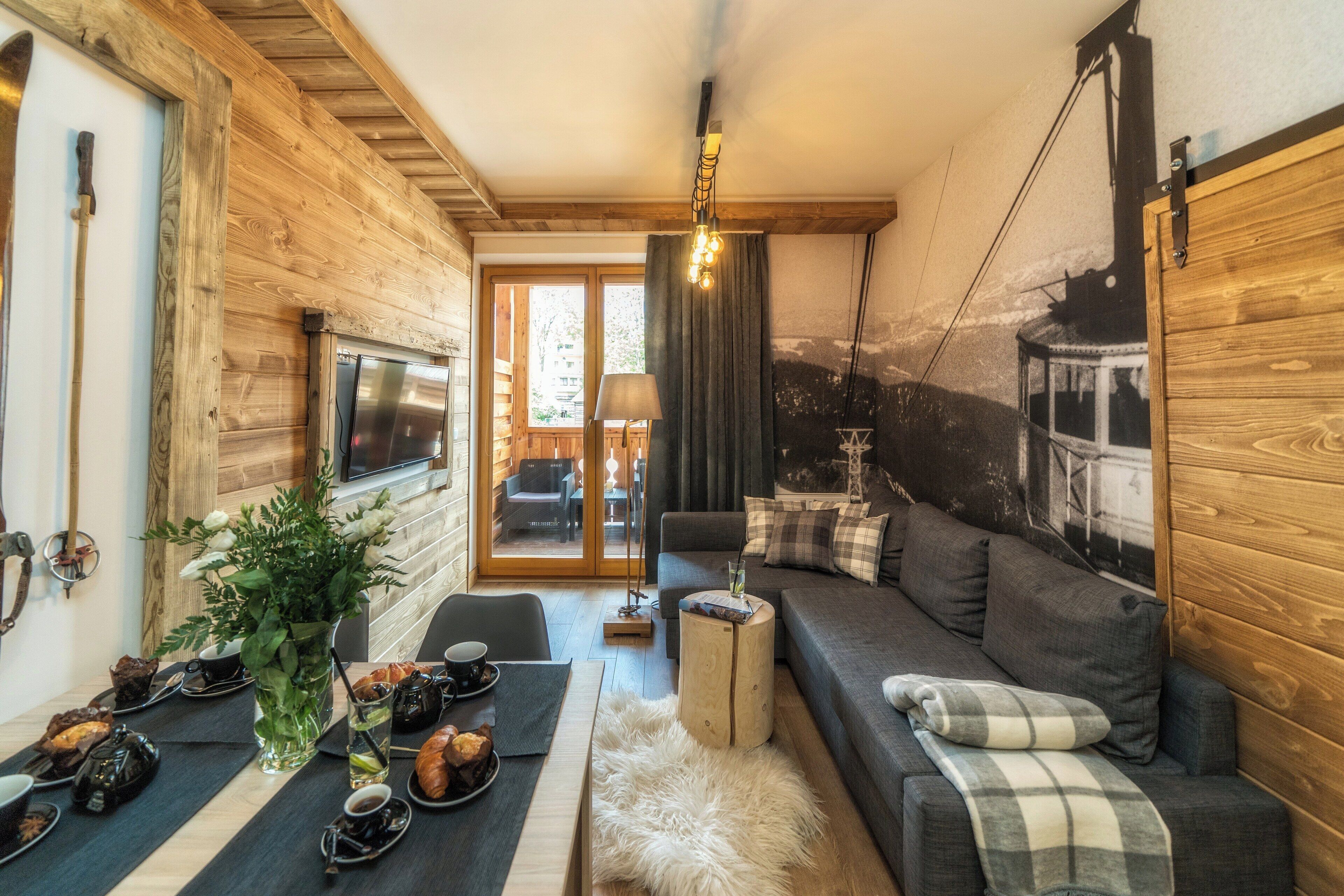 A cozy living room with a sofa, a dining table with a vase of flowers, and a large window.