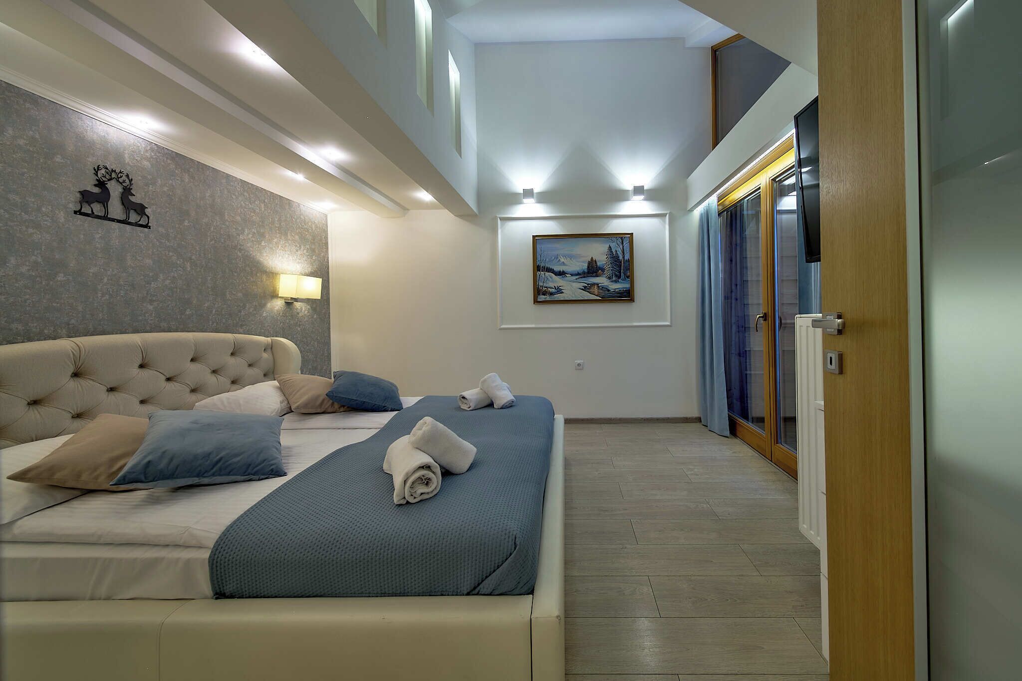 A bedroom with a large bed, a wall-mounted painting, and a wooden door.
