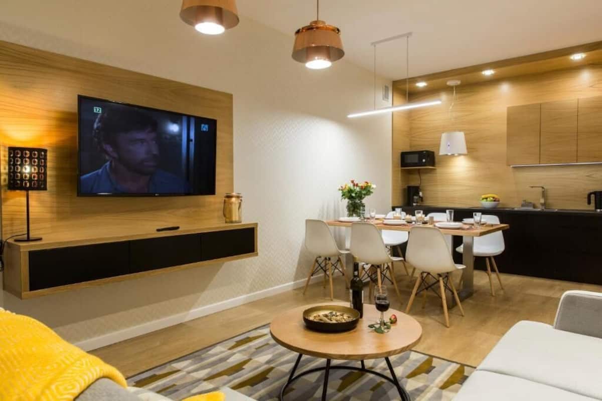 A modern living room with a TV, dining area, and kitchen.