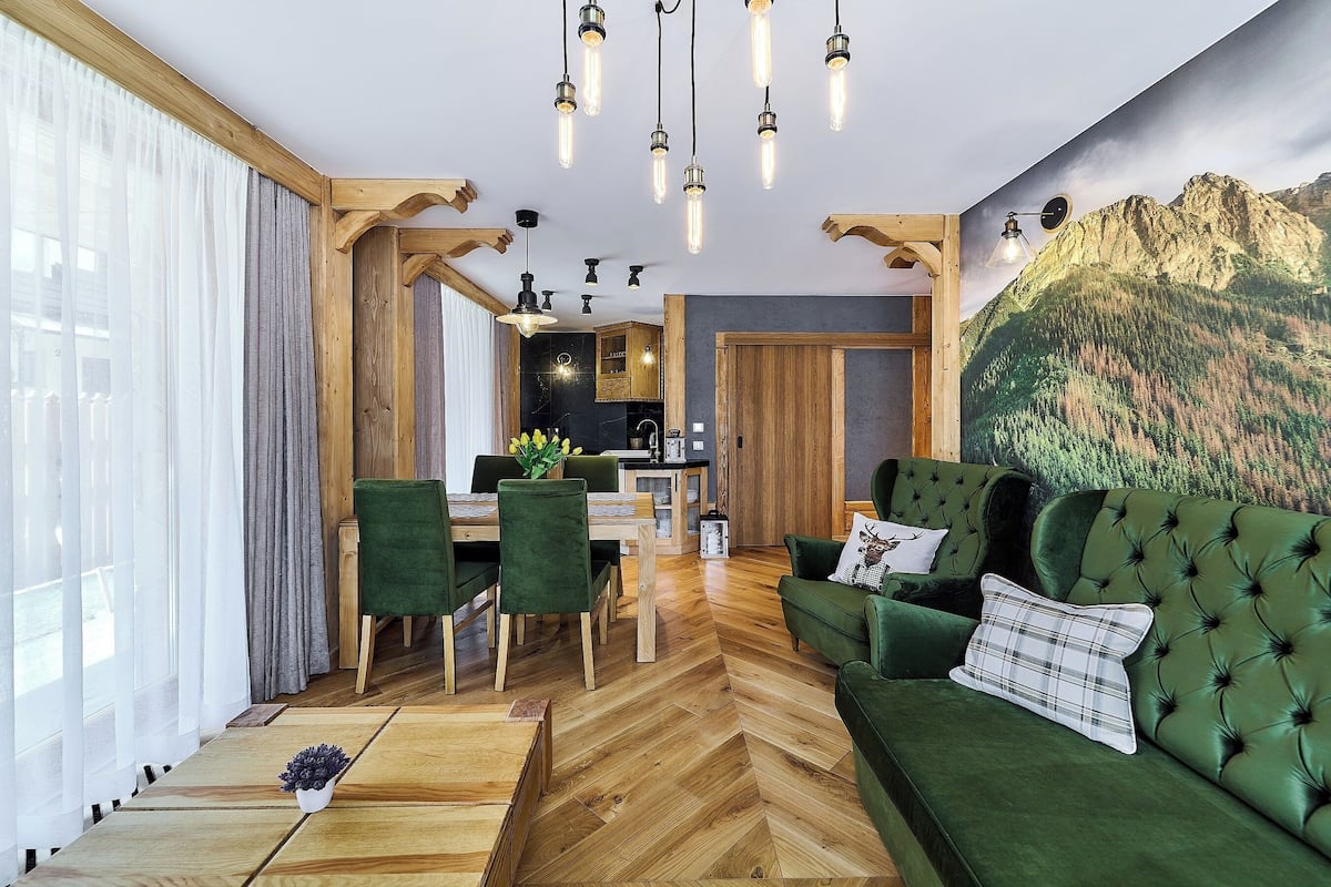 A modern living room with a green sofa, wooden flooring, and a mountain mural.