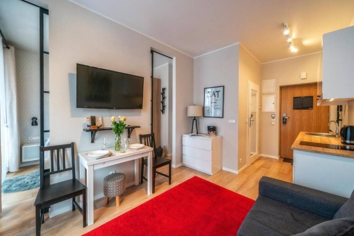 A compact living space with a dining area, kitchenette, and a TV mounted on the wall.