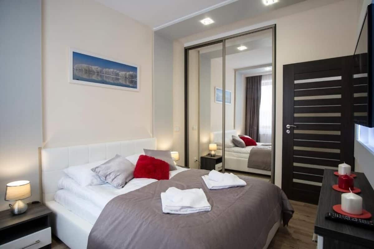 A hotel room with a bed, bedside tables, a mirror, and a TV.