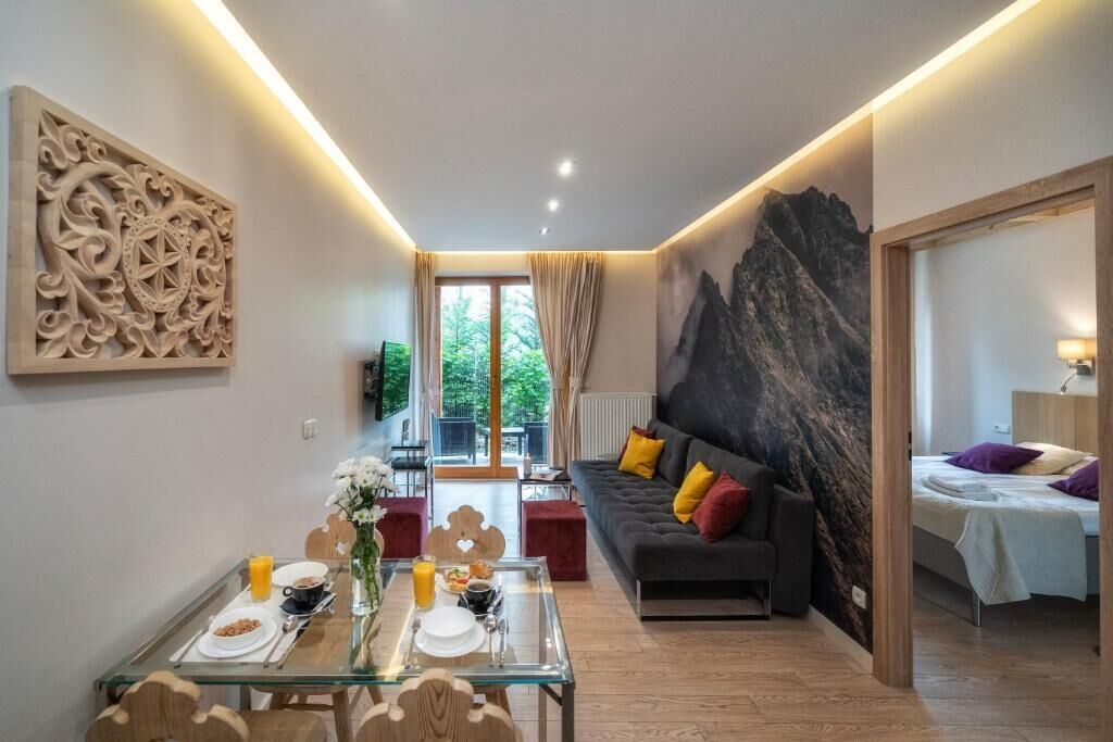 A modern living room with a glass dining table, a sofa with colorful cushions, and a large abstract wall mural.