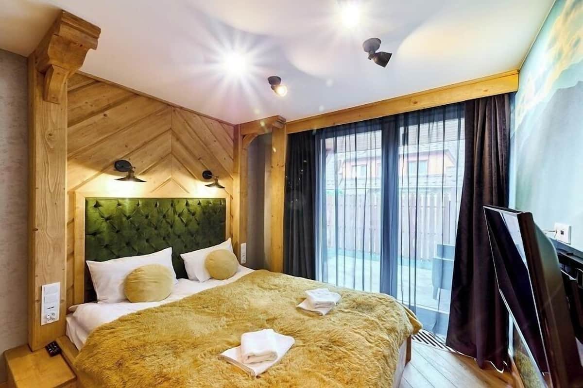 A hotel room with a large bed, wooden headboard, and a view of the outside through large windows.