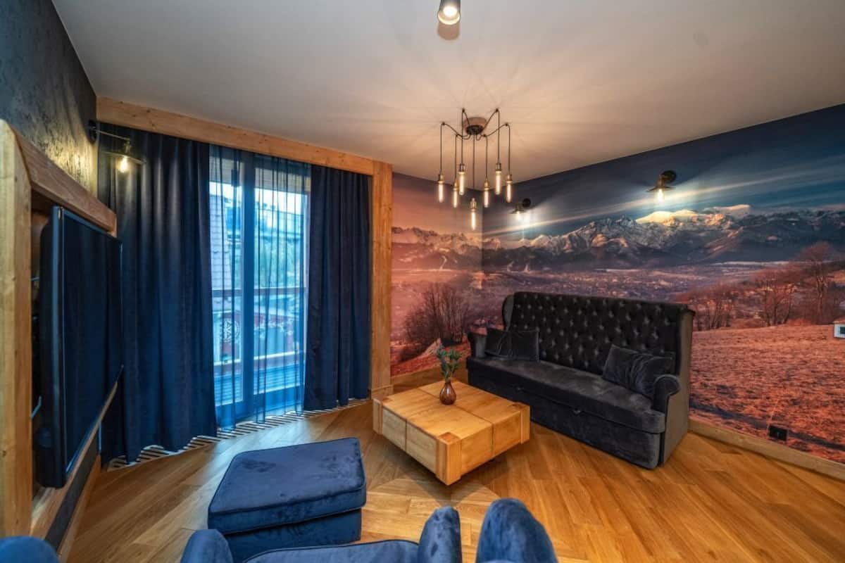 A living room with a sofa, coffee table, and a mural of a mountainous landscape.