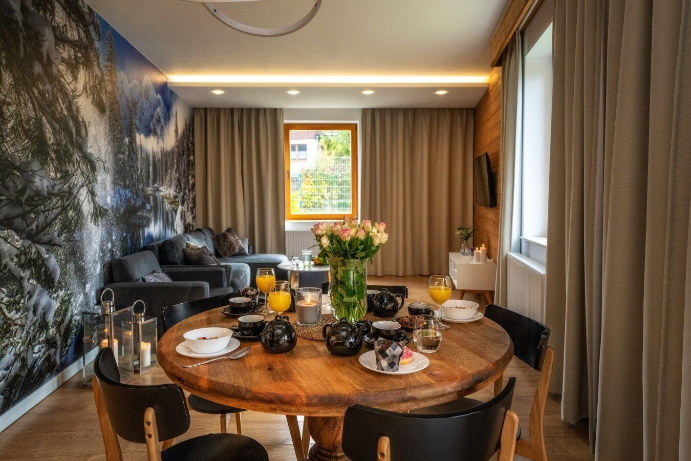 Un comedor moderno con una mesa redonda de madera, sillas negras y una zona de estar acogedora con un sofá y cojines.